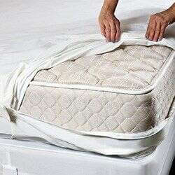 A person is covering a mattress with a protective white cover, ensuring it's snug on the quilted, patterned surface—an essential step in pest control service in Bergen County, NJ. Hands diligently adjust the cover to keep the mattress shielded from unwanted intruders.